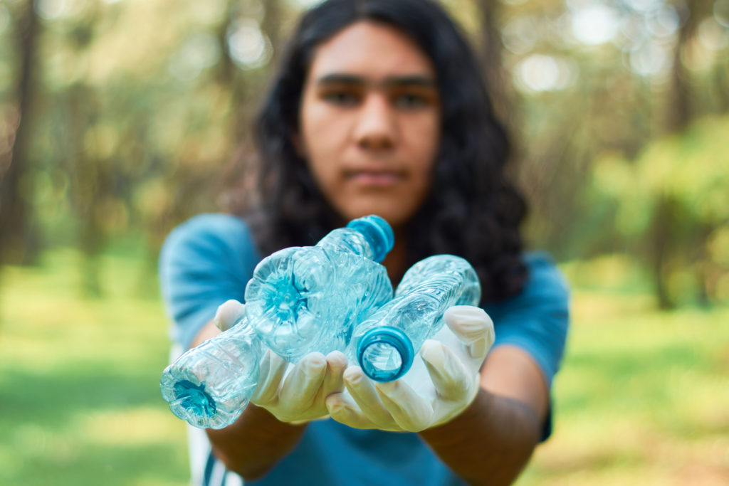 Ethnic gen z male volunteer collects plastic bottle from the forest. Environmental awareness concept.