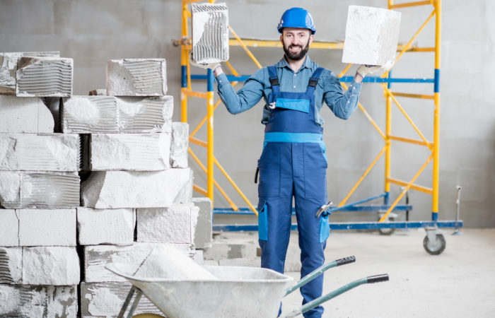 Portrait of a strong builder in uniform holding blocks at the construction site indoors Builder with blocks indoors